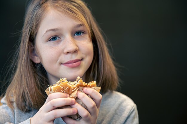 Una niña con pecas come una hamburguesa
