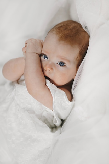 Foto gratuita la niña pelirroja está acostada sobre la manta blanca con grandes ojos azules claros y cubriéndose la cara con pequeños brazos