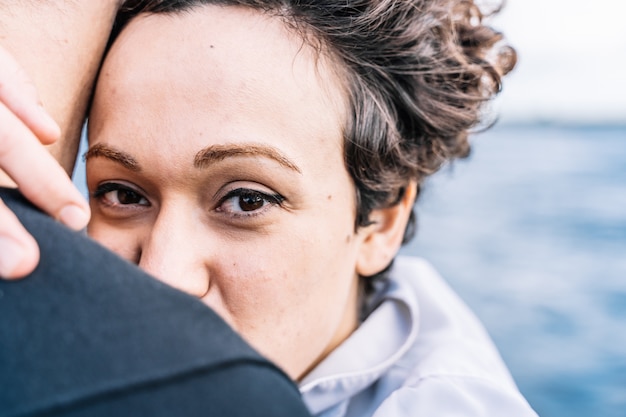 Niña con el pelo rizado mirando hacia adelante mientras abraza a su pareja con el mar desenfocado