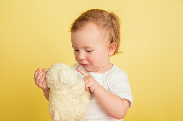 Niña con peluche aislado en la pared amarilla del estudio