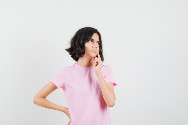 Niña pensando mientras mira a otro lado en camiseta rosa y luce sensata, vista frontal.