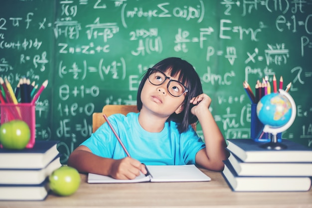 Niña pensativa con el libro cerca de una junta escolar