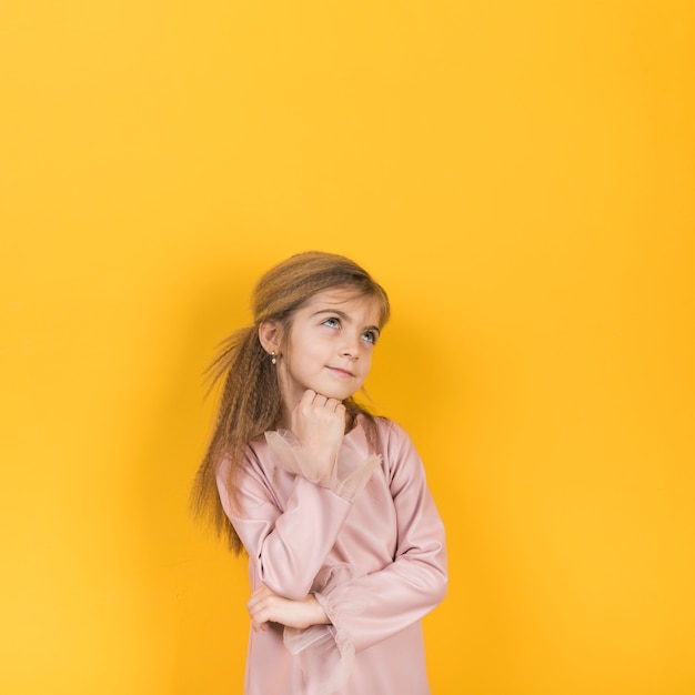 Niña pensativa que mira para arriba en fondo amarillo