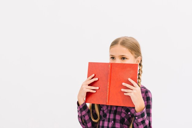 Niña pequeña adorable escondiéndose tras un libro