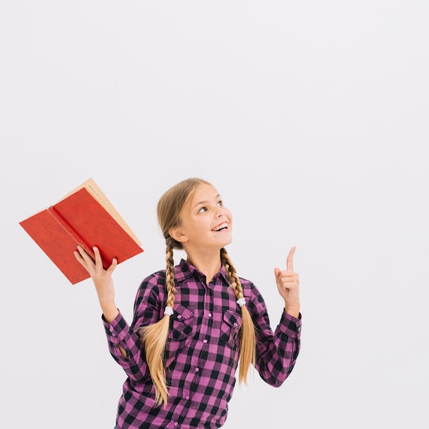 Niña pequeña adorable con un libro señalando hacia arriba