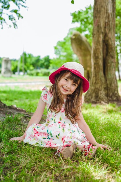 Niña pequeña adorable sentada en el suelo de un parque con un sombrero