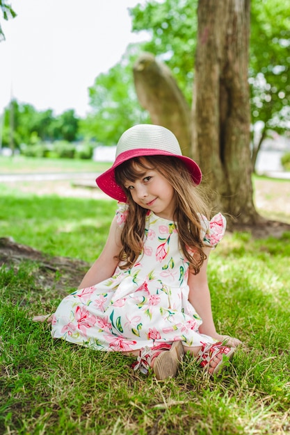 Niña pequeña adorable sentada en el suelo de un parque con un sombrero