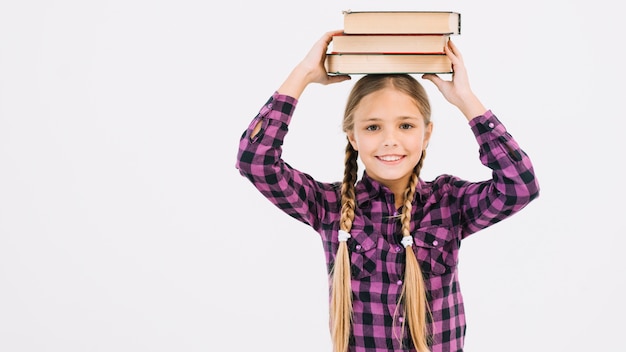 Foto gratuita niña pequeña adorable sosteniendo libros sobre la cabeza