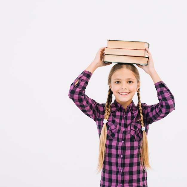 Niña pequeña adorable sosteniendo libros sobre la cabeza