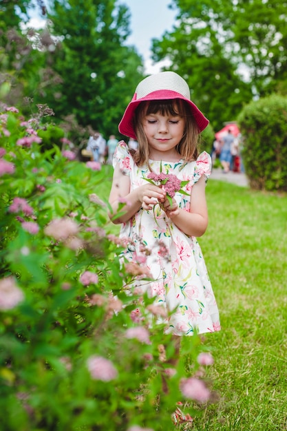 Niña pequeña detrás de un seto con flores en una mano