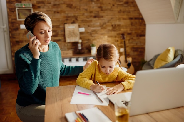 Niña pequeña dibujando en el papel mientras su madre habla por teléfono en casa