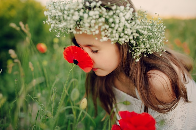 Niña pequeña encantadora oliendo una amapola