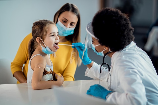 Niña pequeña con examen de garganta en el consultorio del pediatra durante la pandemia de COVID19