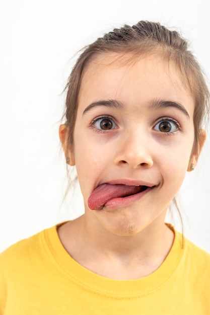 Una niña pequeña hace caras con su lengua colgando en un fondo blanco