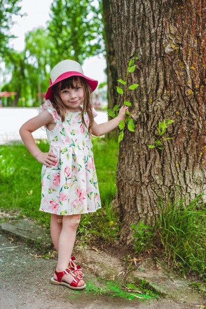 Niña pequeña con una mano apoyada en un árbol