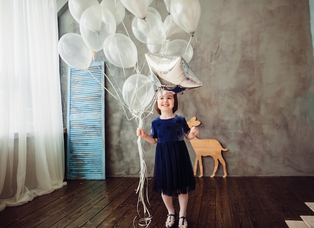 La niña pequeña mantiene globos en la habitación
