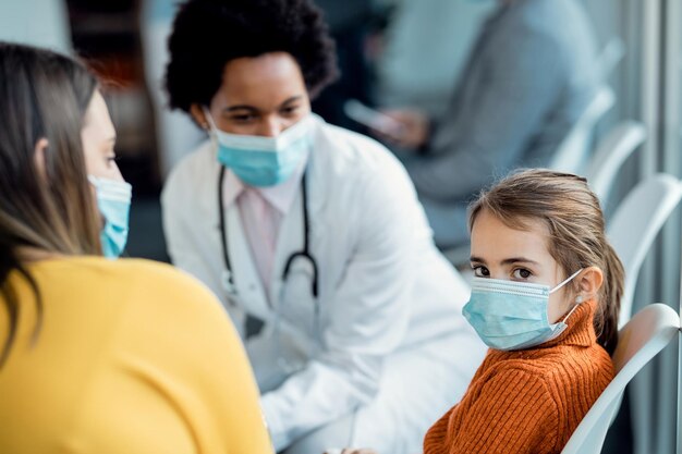 Niña pequeña con mascarilla protectora en una sala de espera en una clínica médica