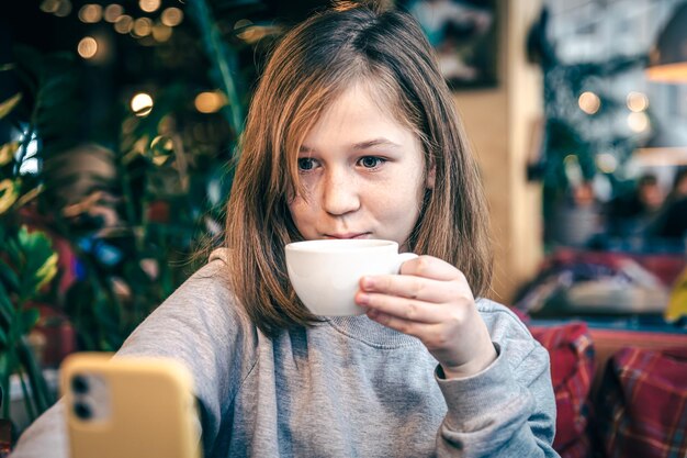 Una niña pequeña mira la pantalla del teléfono inteligente mientras está sentada en un café