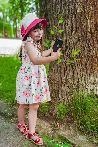 Niña pequeña mirando un smartphone mientras toca un árbol