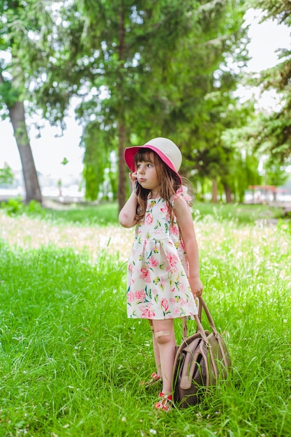 Niña pequeña en un parque hablando por teléfono y con un bolso