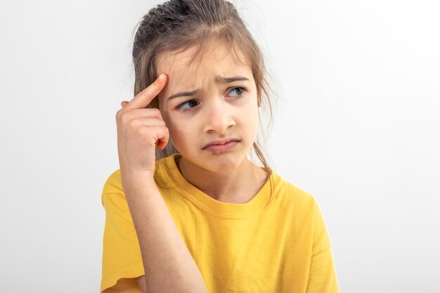 Niña pequeña pensando sosteniendo el dedo en el templo aislado en fondo blanco