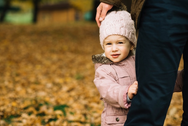 Niña pequeña que se esconde detrás de la pierna adulta