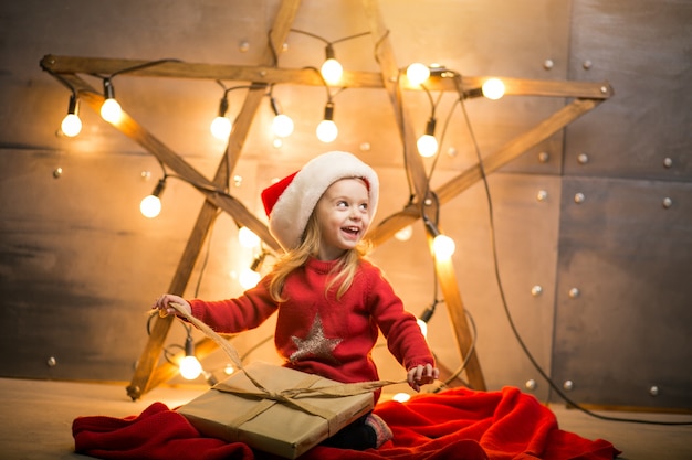 Niña pequeña con regalos en Navidad sentado en manta roja por la estrella