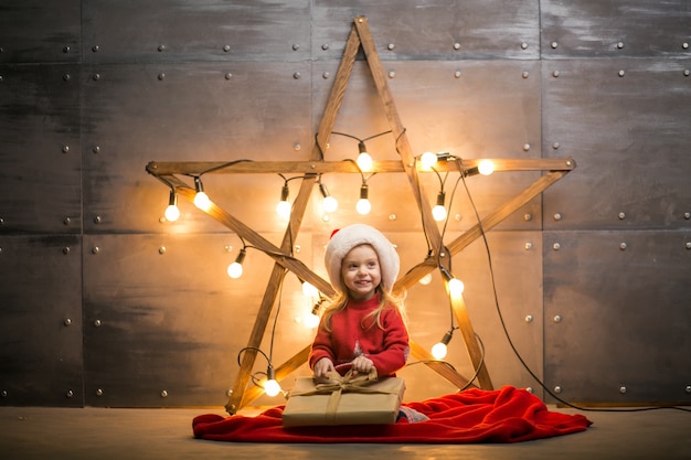 Niña pequeña con regalos en Navidad sentado en manta roja por la estrella