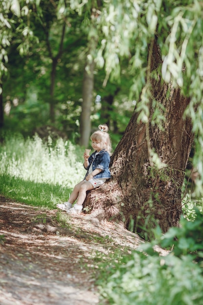 Niña pequeña rubia sentada en un árbol comiéndose un helado