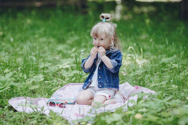 Niña pequeña rubia sentada en una manta de picnic comiendo galletas