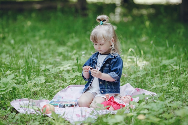 Niña pequeña rubia sentada en una manta de picnic