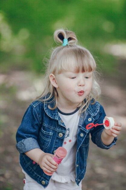 Niña pequeñá rubia soplando por un pompero y haciendo burbujas