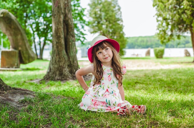 Niña pequeña sentada en el césped con un sombrero