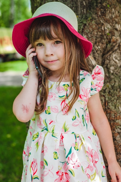 Niña pequeña con sombrero rosa hablando por teléfono