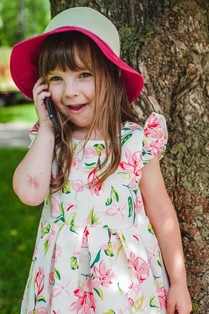 Niña pequeña con sombrero rosa hablando por teléfono