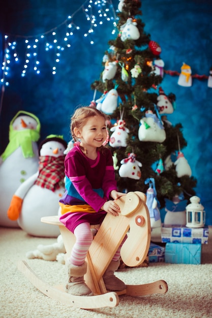 Niña pequeña sonriente al lado del árbol de navidad