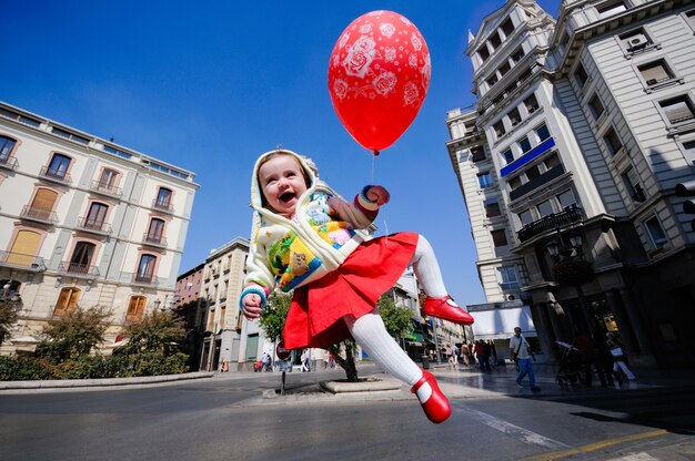 Niña pequeña sonriente volando con un globo en la calle