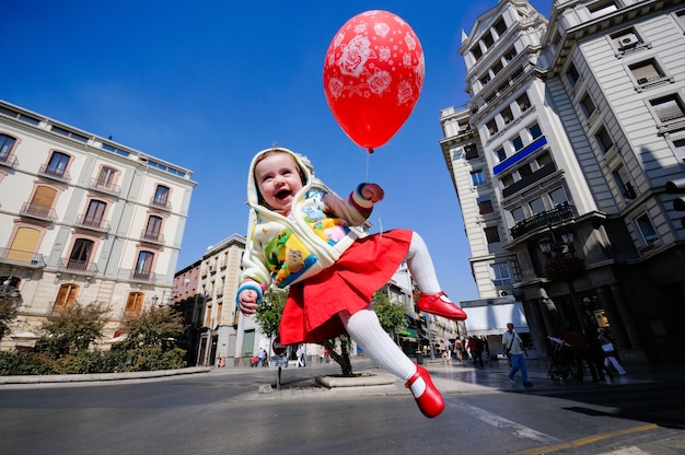 Niña pequeña sonriente volando con un globo en la calle