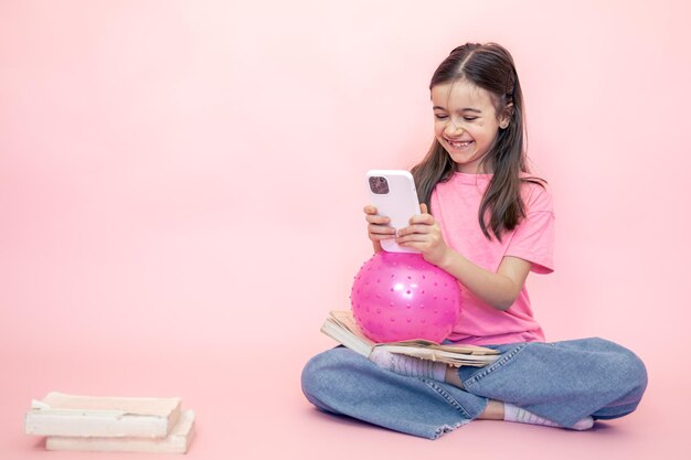 Niña pequeña con un teléfono inteligente en sus manos en un espacio de copia de fondo rosa