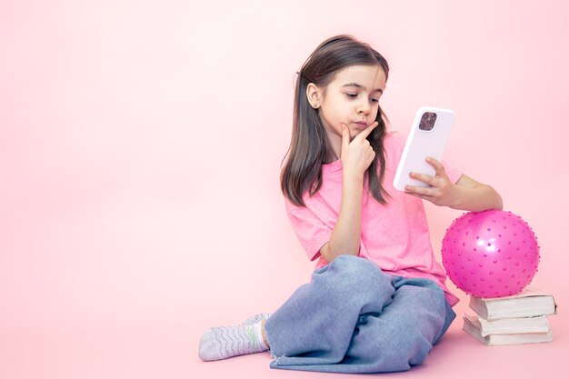 Niña pequeña con un teléfono inteligente en sus manos en un espacio de copia de fondo rosa