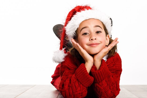 Niña pequeña vestida de papa noel tumbada en el suelo con las manos en la cara