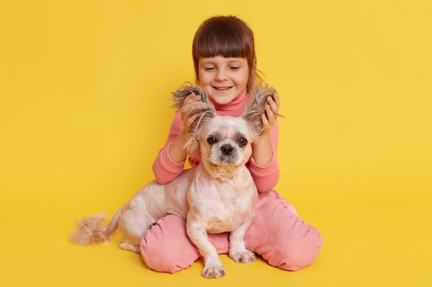 Niña con perro jugando juntos levanta orejas de cachorro y riendo en amarillo