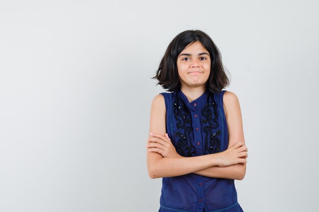 Niña de pie con los brazos cruzados en blusa azul y mirando positivo