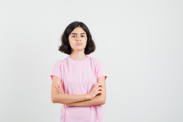 Niña de pie con los brazos cruzados en camiseta rosa y mirando serio, vista frontal.