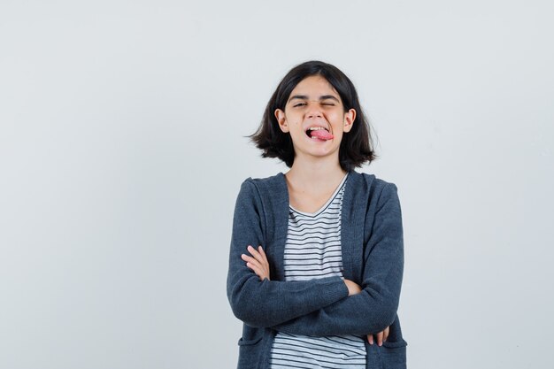 Niña de pie con los brazos cruzados, sacando la lengua en la camiseta