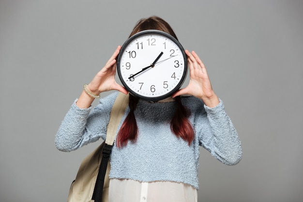 Niña de pie cubriéndose la cara con reloj