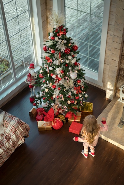 Niña de pie junto a un árbol de navidad festivo