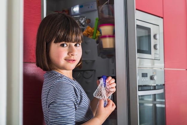 Foto gratuita niña de pie junto a la nevera en la cocina