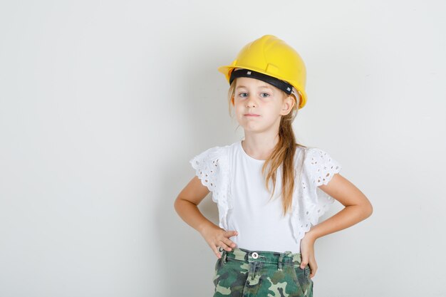 Niña de pie con las manos en la cintura en camiseta blanca