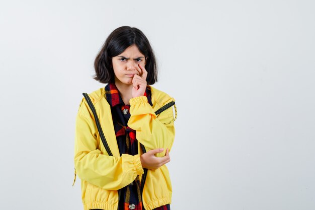 Niña de pie en pose de pensamiento en camisa a cuadros, chaqueta y mirando pensativo